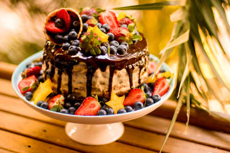 Delicious handmade layered cake decorated with chocolate glaze, strawberries, blueberries, carambola...