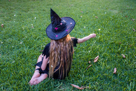 Causcasian blond girl with long hair in halloween witch costume sitting on a green grassの写真素材