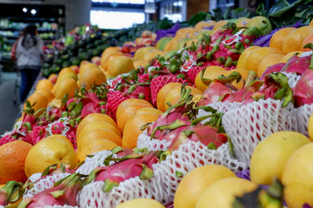 Fruit shop greengrocer display shelf with exotic fruits - mangooes, dragonfruits, oranges, avocadoesの写真素材