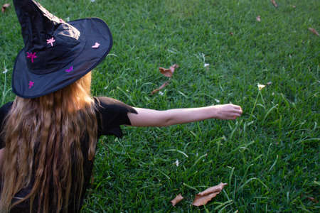 Causcasian blond girl with long hair in halloween witch costume sitting on a green grass