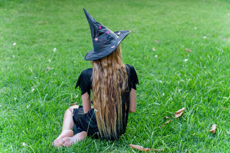 Causcasian blond girl with long hair in halloween witch costume sitting on a green grassの写真素材
