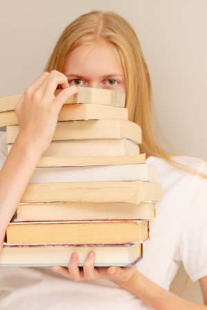 Teenage girl hiding behind big pile of books she wants to read. Booklover or student ready to study conceptの写真素材