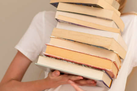 Teenage girl hiding behind the big pile of books. Student life and back to school conceptの写真素材