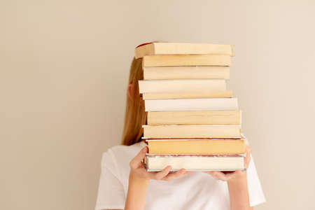 Teenage girl hiding behind big pile of books she wants to read. Booklover or student ready to study conceptの写真素材