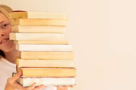 Teenage girl hiding behind the big pile of books. Student life and back to school conceptの写真素材