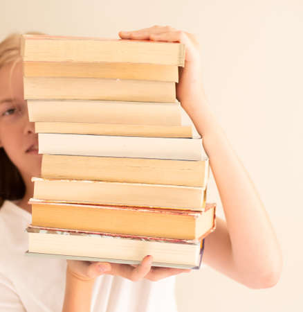 Teenage girl hiding behind the big pile of books. Student life and back to school concept