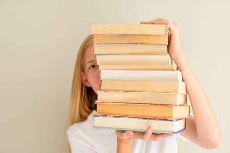 Teenage girl hiding behind big pile of books she wants to read. Booklover or student ready to study conceptの写真素材