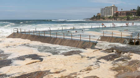 Sydney, Australia 2020-02-15 Ocean storm aftermath: A mass of thick foam covered the rocks following extreme storm weather at Cronulla, NSW, Australia. People are still swimming in a rock poolのeditorial素材