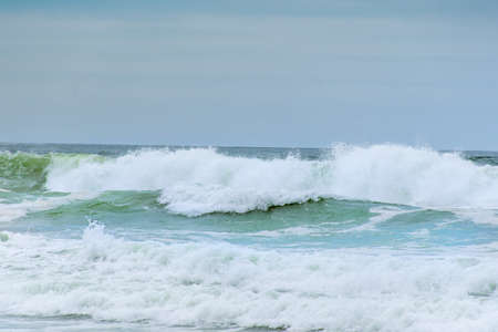 Ocean waves with white foam splashes on a dull cloudy dayの写真素材