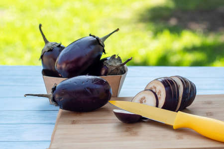 Chopped eggplants aubergines and a yellow knife on cutting board on wooden table. Cooking ingredientsの写真素材