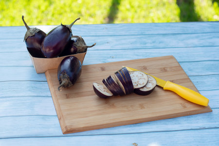 Chopped eggplants aubergines and a yellow knife on cutting board on wooden table. Cooking ingredientsの写真素材