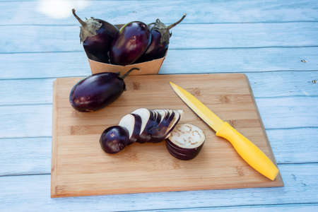 Chopped eggplants aubergines and a yellow knife on cutting board on wooden table. Cooking ingredientsの写真素材