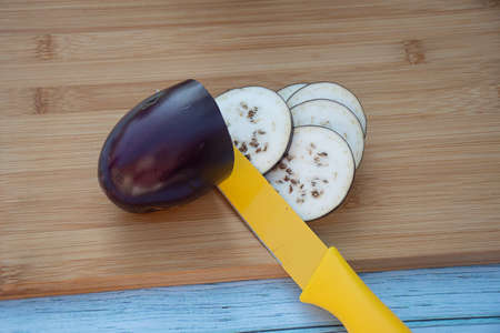 Chopped eggplants aubergines and a yellow knife on cutting board on wooden table. Cooking ingredientsの写真素材