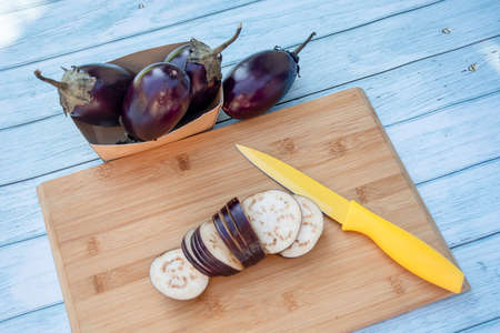 Chopped eggplants aubergines and a yellow knife on cutting board on wooden table. Cooking ingredientsの写真素材