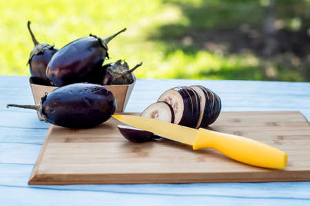 Chopped eggplants aubergines and a yellow knife on cutting board on wooden table. Cooking ingredientsの写真素材
