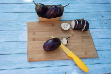 Chopped eggplants aubergines and a yellow knife on cutting board on wooden table. Cooking...