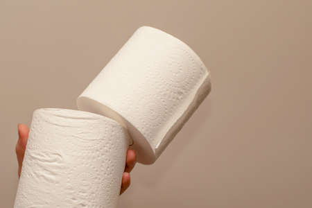 Close up of hands holding two toilet paper rolls on neutral background. Shortage and stockpile concept.の写真素材