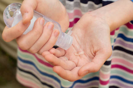A girl in a striped dress applying hand sanitizer on her hands to protect from the coronavirusの写真素材