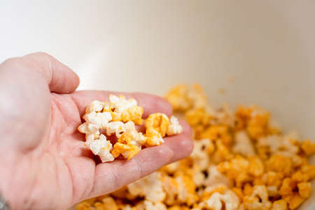 A hand taking fresh made popcorn from a white bowl. Entertainment at home concept. Selective focus on hand.の写真素材