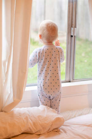 Adorable baby boy staying on the bed and looking through the window. Stay home conceptの写真素材