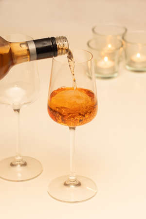 Rose wine pouring from the bottle into glasses on a white table with candles. Romantic celebration concept.の写真素材