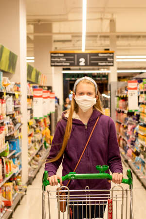 A girl wearing handmade face covering mask with shopping trolley at the supermarket during the COVID-19 pandemic.の写真素材