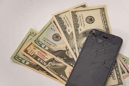 Hand holding a phone with badly smashed screen and US dollars to pay for repair. Accident conceptの写真素材