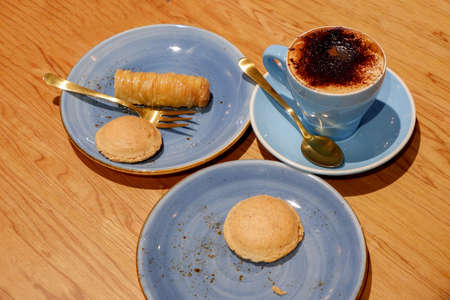 A cup of capucchino coffee with delicious sweets for dessert - amaretti biscuits and pastry finger cigar served on rustic blue plates.の写真素材
