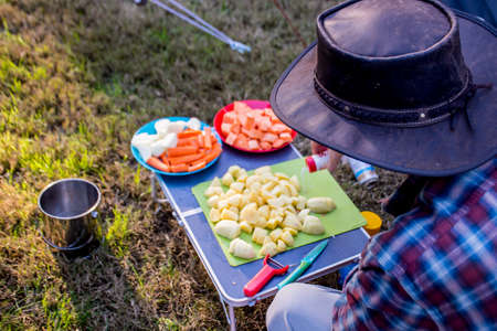 Disfocused shot of camp cooking process. A man preparing vegetables to make a stew on a campfire. Camping life.の写真素材