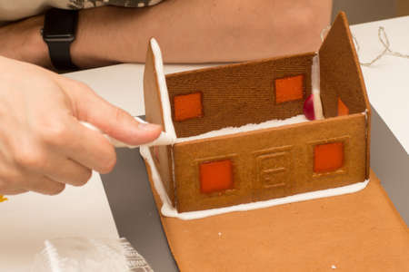 Selective focus shot of building of gingerbread house with royal icing. Windows are made with melted candies.の写真素材