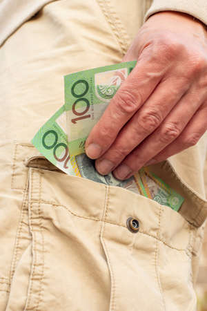 Hand holding australian dollars 100 banknotes in the pocket of cargo shorts. Tradie finance concept.の写真素材