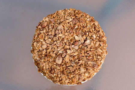 Nut biscuit cake finished with crushed sugar-coated candied caramelized almonds on a glass table.の写真素材