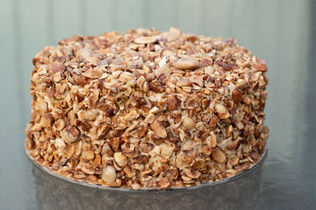 Beatiful nut biscuit cake finished with crushed sugar-coated candied caramelized almonds on a glass table.の写真素材