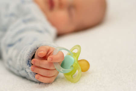 Little baby boy is peacefully sleeping and holding a pacifier dummy in his hand. Selective focus on a dummy.の写真素材
