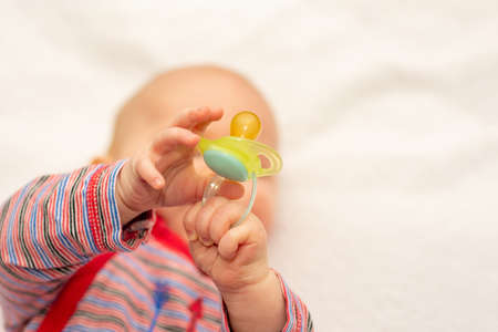 Little baby boy holding a pacifier dummy in his hand and playing with it. Selective focus on a dummyの写真素材