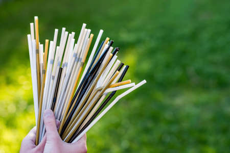 Hand holding a bouquet of plastic straws on green grass background. Plastic pollution, environmental waste. Say no to plastic straws. Save our green planetの写真素材