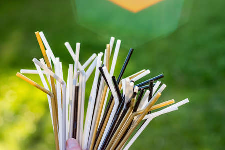 Hand holding a bouquet of plastic straws on green grass background. Plastic pollution, environmental waste. Say no to plastic straws. Save our green planetの写真素材