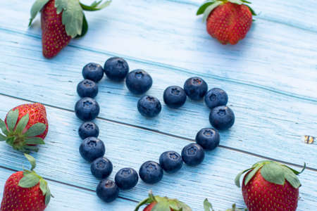Blueberry heart and some strawberries on a wooden background. Valentines day concept.