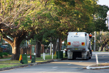 Sydney, Australia - 2019-09-26 Australian garbage wheelie bins with colourful lids for recycling and general household waste lined up on the street kerbside for council rubbish collection and a garbage truck on duty.のeditorial素材