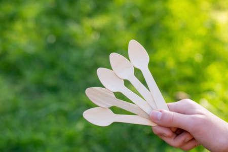 Hand holding disposable wooden teaspoon on a green grass background. Reduce Reuse Recycle. Say no to...