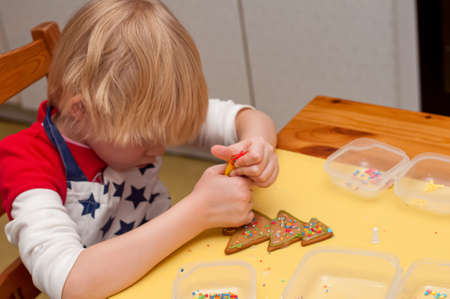 A girl decorates fresh baked homemade Chritstmas gingerbread cookie with icing and sprinkles. Selecrive focusの写真素材
