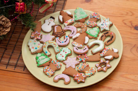 Fresh baked homemade Chritstmas gingerbread cookies decorated with icing and sprinkles undere a branch of Christmas tree. Selective focusの写真素材