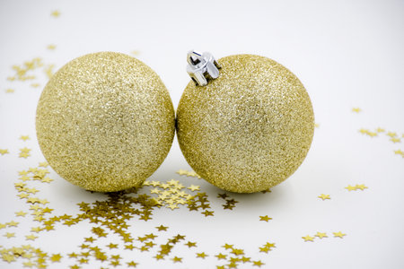 Two golden christmas balls baubles on a white background with blurry golden stars. Festive season backgroundの写真素材
