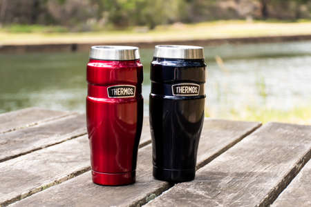 Sydney, Australia - 2020-11-21 Thermos 470ml Insulated Reusable Stainless Steel travel tumbler mugs on the table with nature backgroundのeditorial素材