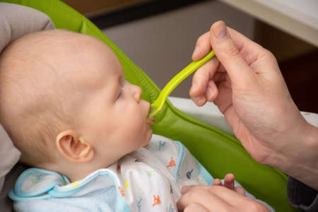 Adult feeding 6 months old little baby boy with first solid food. Giving a spoon with broccoli baby...