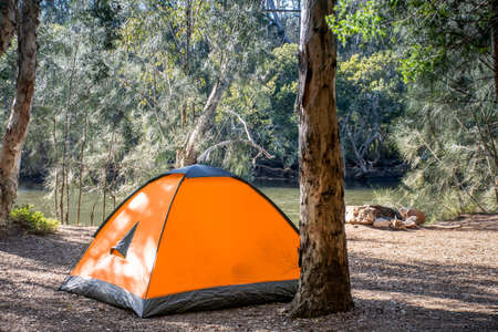 Orange tent at the campsite surrounding by nature on the river bank. Camping and recreationの写真素材