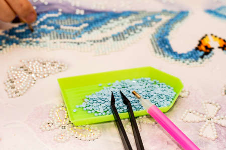 Diamond painting embroidery craft. Acrylic rhinestones, pen and tweezers. Closeup, selective focus.の写真素材