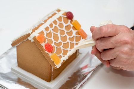 Decorating of gingerbread house with royal icing and sweets. Christmas family moment. Homemadeの写真素材