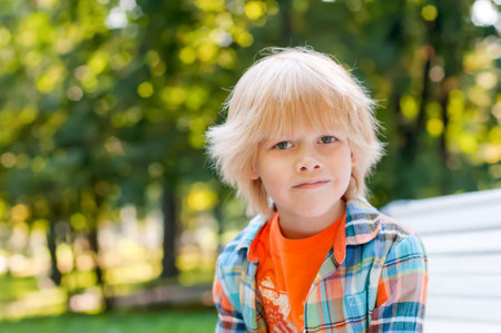 Cute blonde caucasian kid sitting on the bench at the park. Summer vacation happy childhood conceptの写真素材