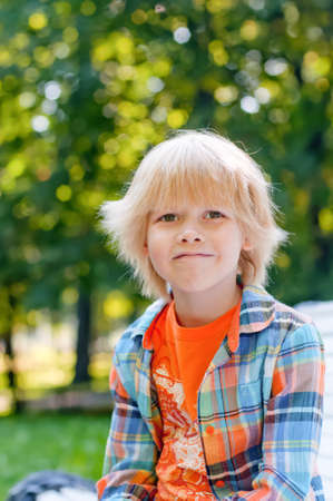 Cute blonde caucasian kid sitting on the bench at the park. Summer vacation happy childhood conceptの写真素材